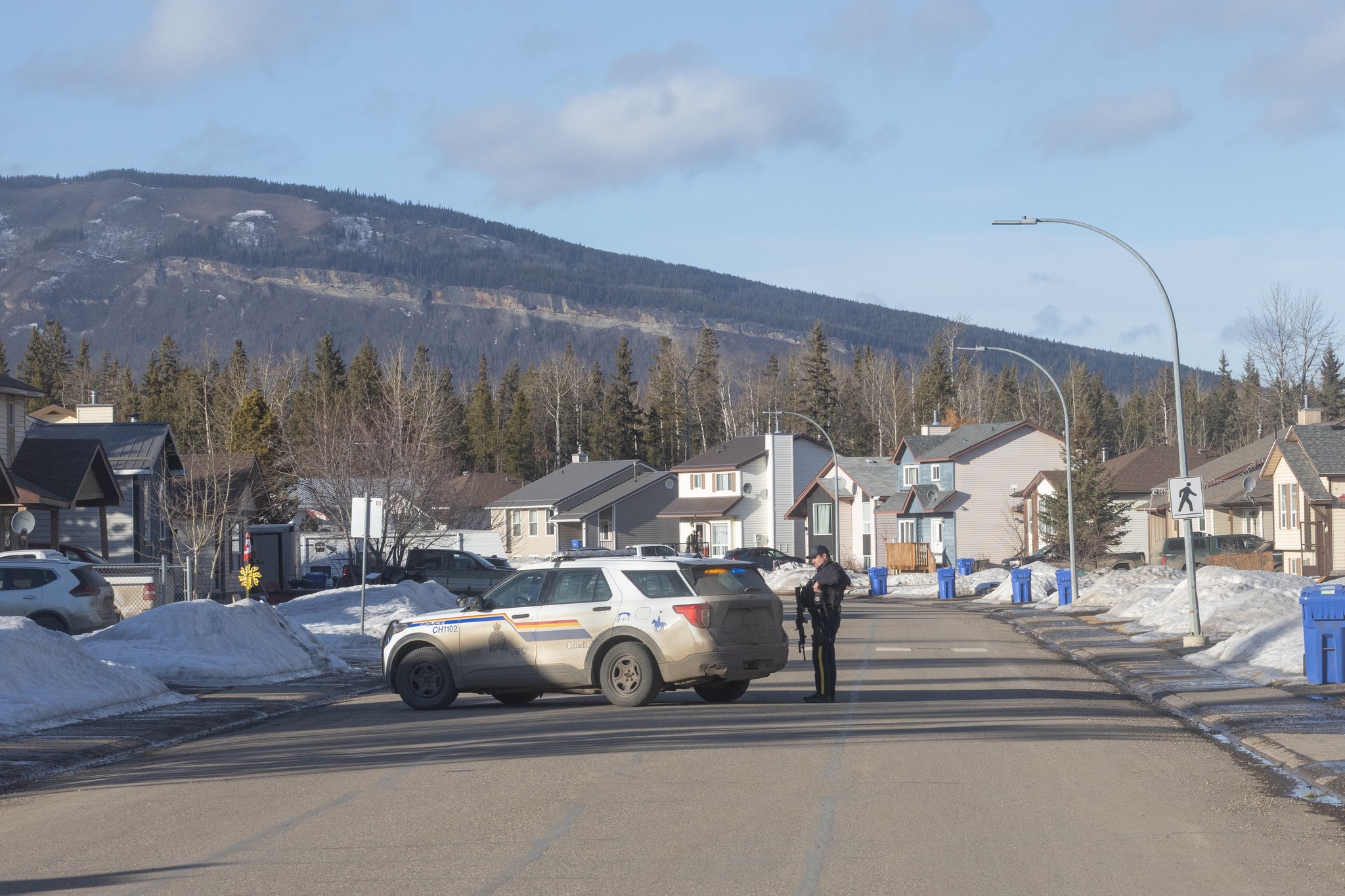 An RCMP officer stands on a road beside an RCMP SUV